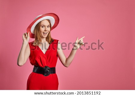 Young girl on pink wall background. Woman showing copyspace pointing. Girl wearing hat and red stylish clothes.