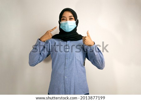Muslim woman wearing medical mask, with ok sign hand, success sign, good work sign, victory sign, concept of preventing covid-19, concept of preventing corona virus, isolated on gray background