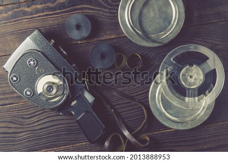 Old amateur movie camera, spools of roll film and reel of film stock on dark wooden background