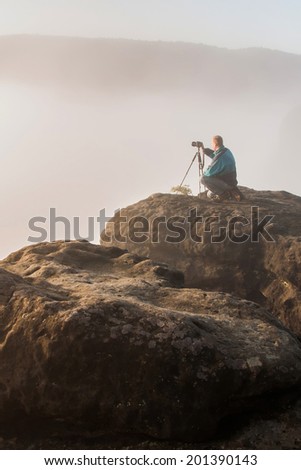 Photographer with the digital camera and tripod on the sandstone rock in the morning  national park Saxon Switzerland in Germany
