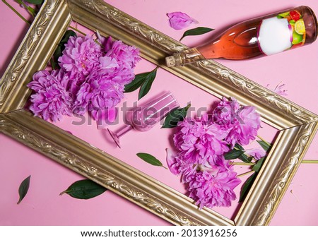 A creative composition with pink wine and a stylish glass of wine. pink peonies and an old vintage frame give the composition a special charm. Flat layout, top view, a place to copy.