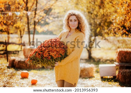 Beautiful curly girl holds an armful of orange autumn flowers against the background of the autumn fair. High quality photo