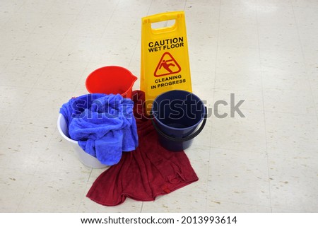 Caution slippery floor sign beside buckets and towels on a wet floor from roof leaking. No people. Copy space