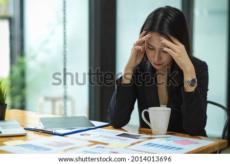 Attractive businesswoman getting stressed out from work with financial reports, tablet, laptop, coffee cup on wood desk at office