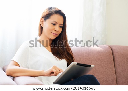 Positive beautiful young woman sitting on sofa at home and working on laptop, quarantine and distant work concept