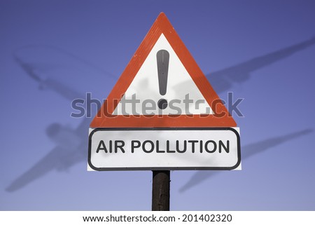 White road warning triangle with black  exclamation point and red frame on  a wooden mast in front of a blue sky. A second rectangular sign warns in english about  air pollution