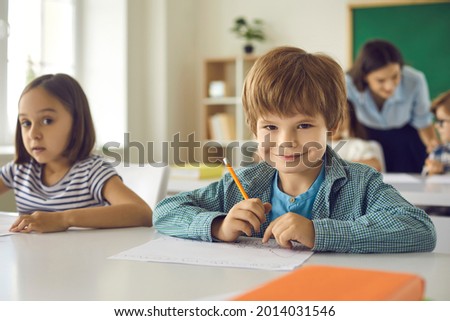 Happy student on his first day at school. Portrait of an adorable elementary school boy in the classroom. Cute little child sitting at his desk, holding a pencil, smiling and looking at the camera Royalty-Free Stock Photo #2014031546