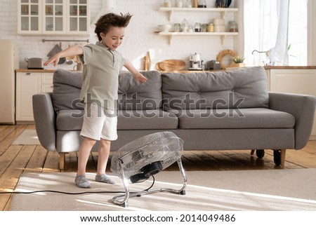 Little preschool boy enjoy fresh air flow from fan. Cute small kid play with ventilator blowing cool wind alone in living room at home. Cute child have fun indoors in apartment one. Childhood leisure Royalty-Free Stock Photo #2014049486