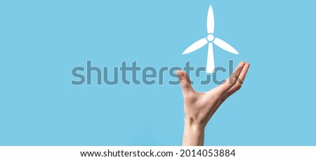 Hand holding an icon of a windmill that produces environmental energy on blue background