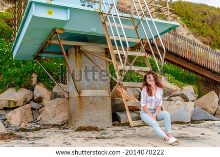 A beautiful young woman is relaxing on the beach in San Diego, a view of the blue lifeguard tower.