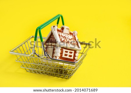 House in metal shopping basket on yellow background, concept of buying an apartment or house