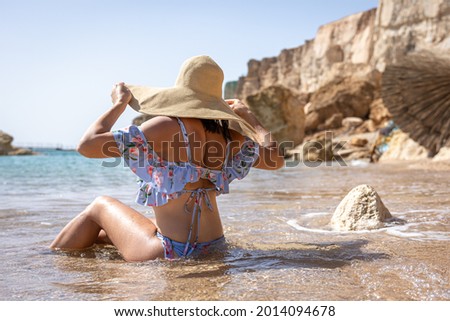A woman in a big hat sunbathes on the beach near the sea.