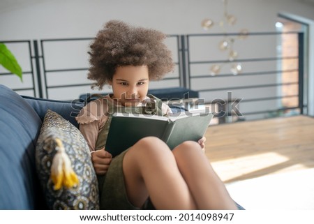 Little smart girl reading book on sofa