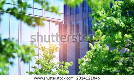 Eco architecture. Green tree and glass office building. The harmony of nature and modernity. Reflection of modern commercial building on glass with sunlight.  Royalty-Free Stock Photo #2014121846