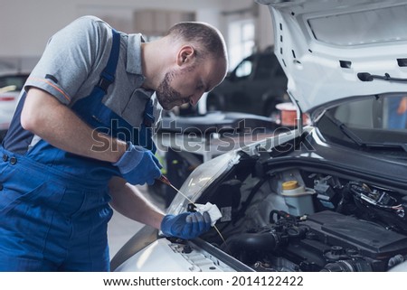 Mechanic doing a vehicle inspection, he is checking a car's oil level and quality using a dipstick Royalty-Free Stock Photo #2014122422