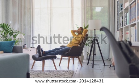 Indian man relaxing in the living room at home and listening to music, he is sitting on an armchair and wearing wireless headphones Royalty-Free Stock Photo #2014128431