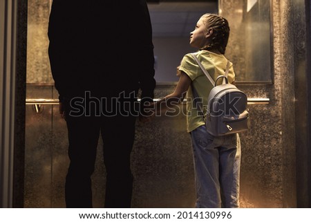 Rear view on unrecognizable man with child standing in lift, kidnapping children concept. copy space. view from back. little girl is very gullible, don't afraid of adult man, holding hands together