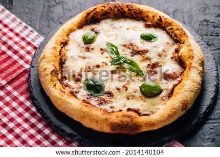 Traditional pizza on a black rustic background with basil, tomato, mozzarella, olive oil and red plaid tablecloth
