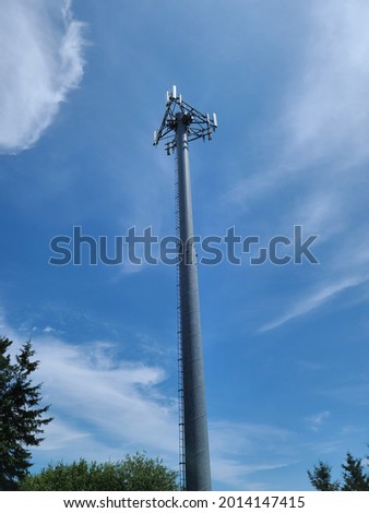 Looking up at a large, thin cell phone tower in the middle of the wilderness. The tower is metal and grated. It goes all the way up into the sky. 