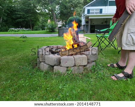 The view of a backyard fire pit. The The fire is lit and is burning shredded paper while igniting boards in the round, cinder block fireplace. Royalty-Free Stock Photo #2014148771