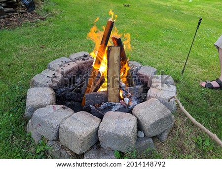 The view of a backyard fire pit. The The fire is lit and is burning shredded paper while igniting boards in the round, cinder block fireplace. Royalty-Free Stock Photo #2014148792
