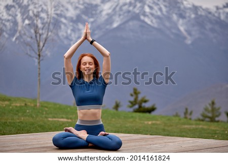 Redhead Woman Exercise outdoors. Fit Female practicing yoga pose, keep balance, body vital zen meditation in nature, mountains Landscape outdoor in the background. Healthy lifestyle