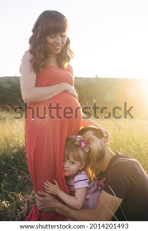Dad and daughter are looking at a pregnant belly. The family is expecting a second child. The little sister is waiting for her brother. Loving relatives kiss and stroke the pregnant belly