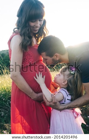 Dad and daughter are looking at a pregnant belly. The family is expecting a second child. The little sister is waiting for her brother. Loving relatives kiss and stroke the pregnant belly
