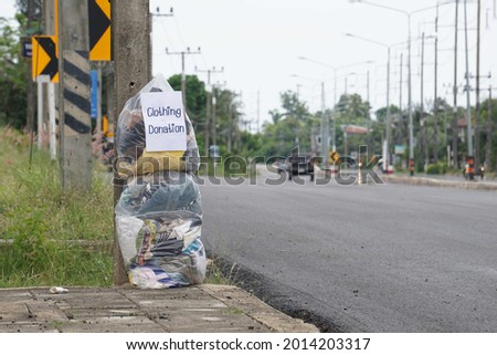 Used clothes are placed in plastic bags piled up on the roadside, and there are signs saying they are given away for free to those in need. clothing donation concept.