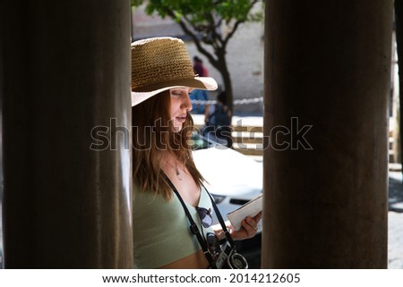 Young and pretty girl with red hair is looking at the map of the city. The girl is wearing a hat and carrying a camera. Travel and holiday concept.