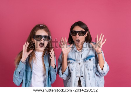 Modern mom and daughter in denim jackets on terracotta background in 3d cinema glasses watching horror movie together, scared afraid face