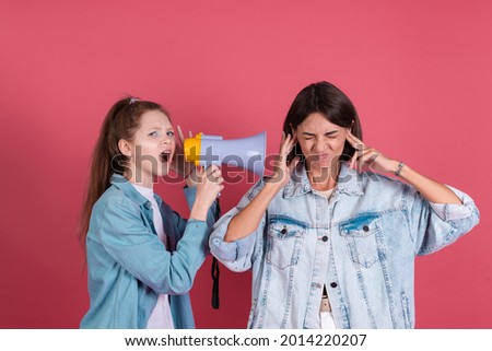 Modern mom and daughter in denim jackets on terracotta background girl shouting in megaphone mom stand by with ears cover with fingers