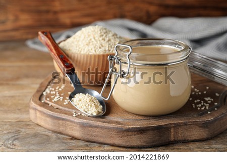 Jar of tasty sesame paste and seeds on wooden table Royalty-Free Stock Photo #2014221869