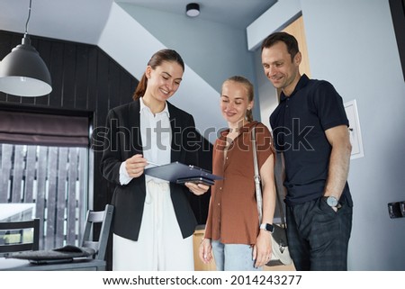 Waist up portrait of happy young couple talking to real estate agent while buying new house, copy space