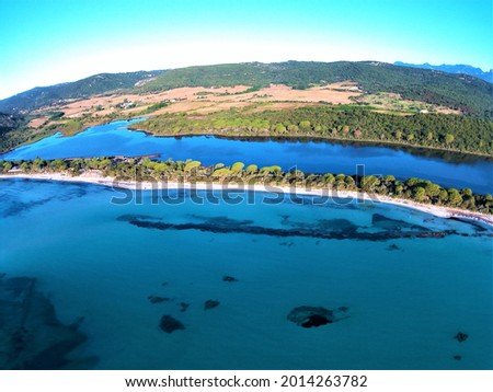 Picture captured by drone of a beautiful beach of white sand and transparent water located in Corsica with mountains and a lake surrounded by a large forest.
