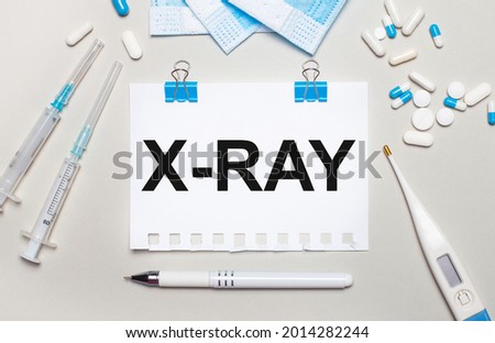 On a light gray background, blue medical masks, syringes, an electronic thermometer, pills, a pen and a notebook with the inscription X-RAY. Medical concept