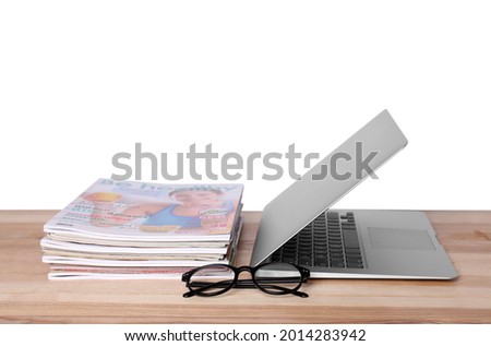 Laptop, glasses and stack of magazines on wooden table