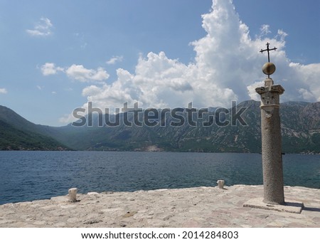 A stone post with a cross at the top is on the pier on the background of the mountains
