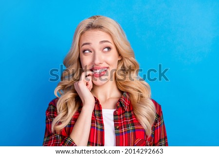 Photo of sweet tricky young woman dressed checkered shirt smiling biting finger looking empty space isolated blue color background