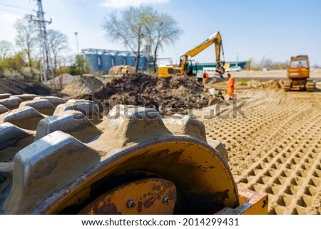 View on road roller with spikes vibrating, compactor is compacting, tamping sand for road foundation at building site. Royalty-Free Stock Photo #2014299431