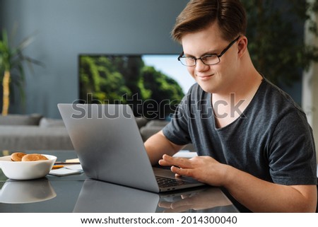 Smiling white young man with down syndrome using laptop computer at home sitting at the table Royalty-Free Stock Photo #2014300040