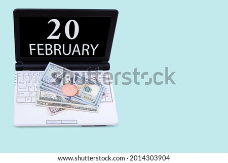 20th day of february. Laptop with the date of 20 february and cryptocurrency Bitcoin, dollars on a blue background. Buy or sell cryptocurrency. Stock market concept. Winter month, day of the year