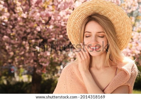 Happy stylish young woman near blossoming sakura tree outdoors. Spring look