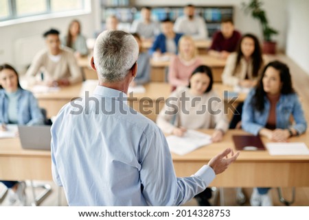 Back view of mature teacher talking to his students during lecture at college classroom. Royalty-Free Stock Photo #2014328753