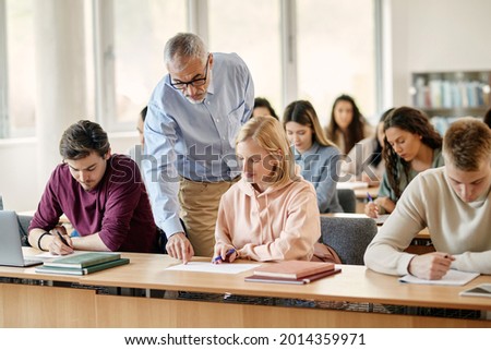 Mature professor talking to his student while assisting her on a class at the university.  Royalty-Free Stock Photo #2014359971