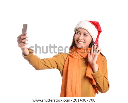 Happy young woman in Santa hat taking selfie on white background