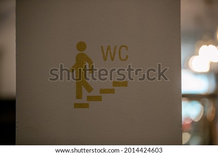 A closeup shot of a sign showing the bathroom on a white wall