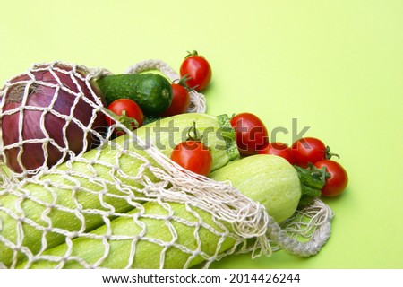 Ripe juicy red tomatoes, green cucumbers and zucchini in a string bag.