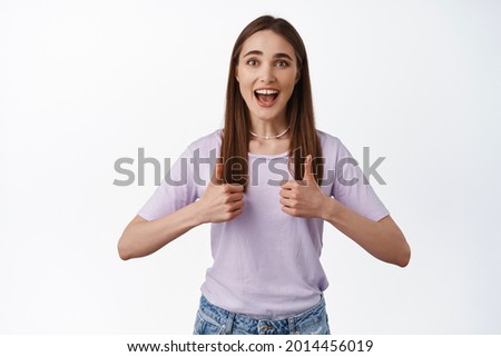 Wow thats good. Beautiful young woman shows her support, great work, nice job gesture, thumbs up and smile, encourage you, praise effort, standing over white background