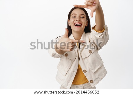 Taking picture of you. Happy attractive woman laughing, smiling and looking through hand frames, making camera shot to remember moment, creating picture, white background